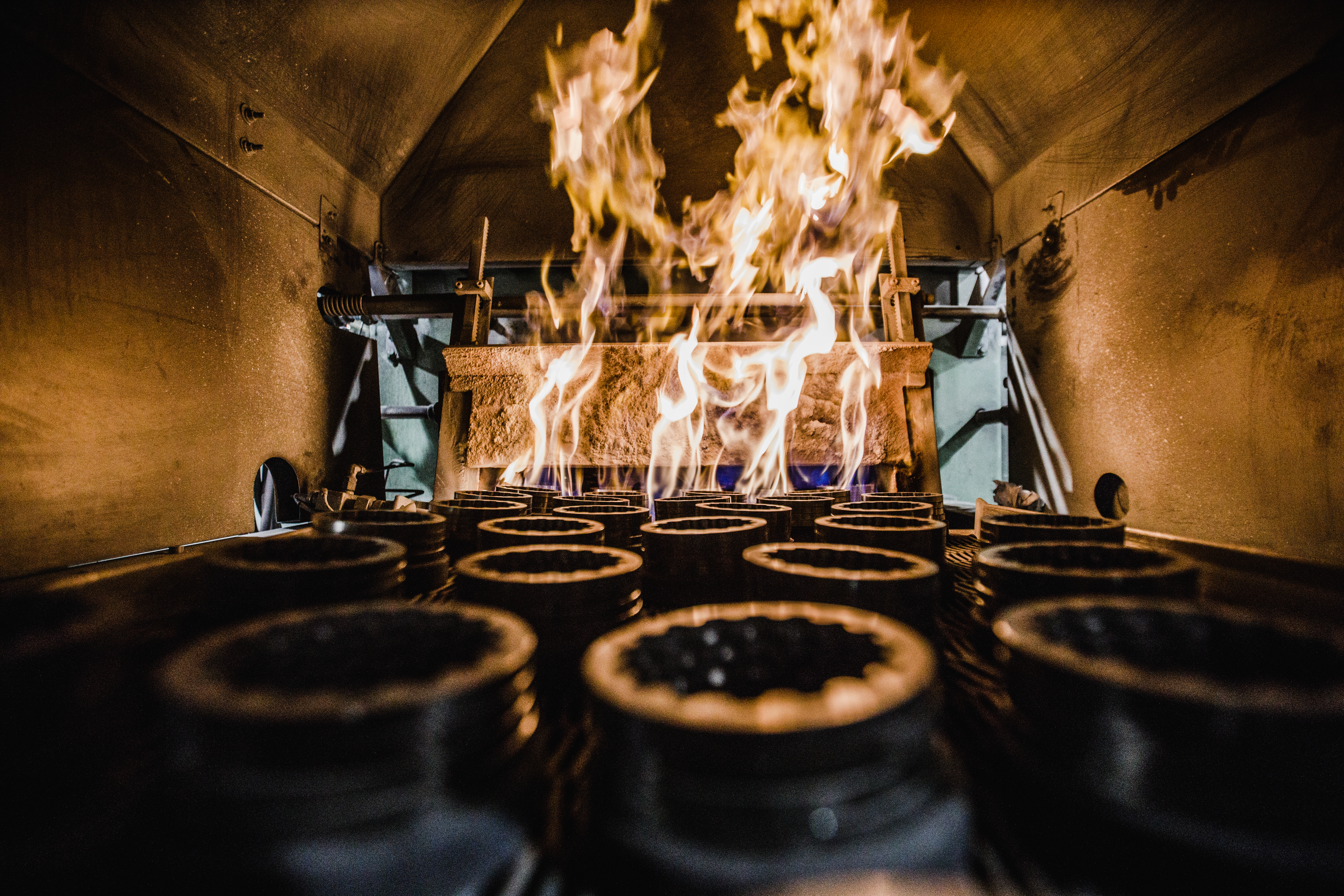 Sintering process taking place, rows of stainless steel parts move through industrial furnace as tall flames rise around them