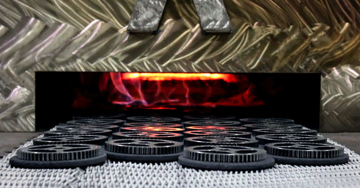 Close up of metal parts on a conveyor moving toward a glowing industrial furnace 